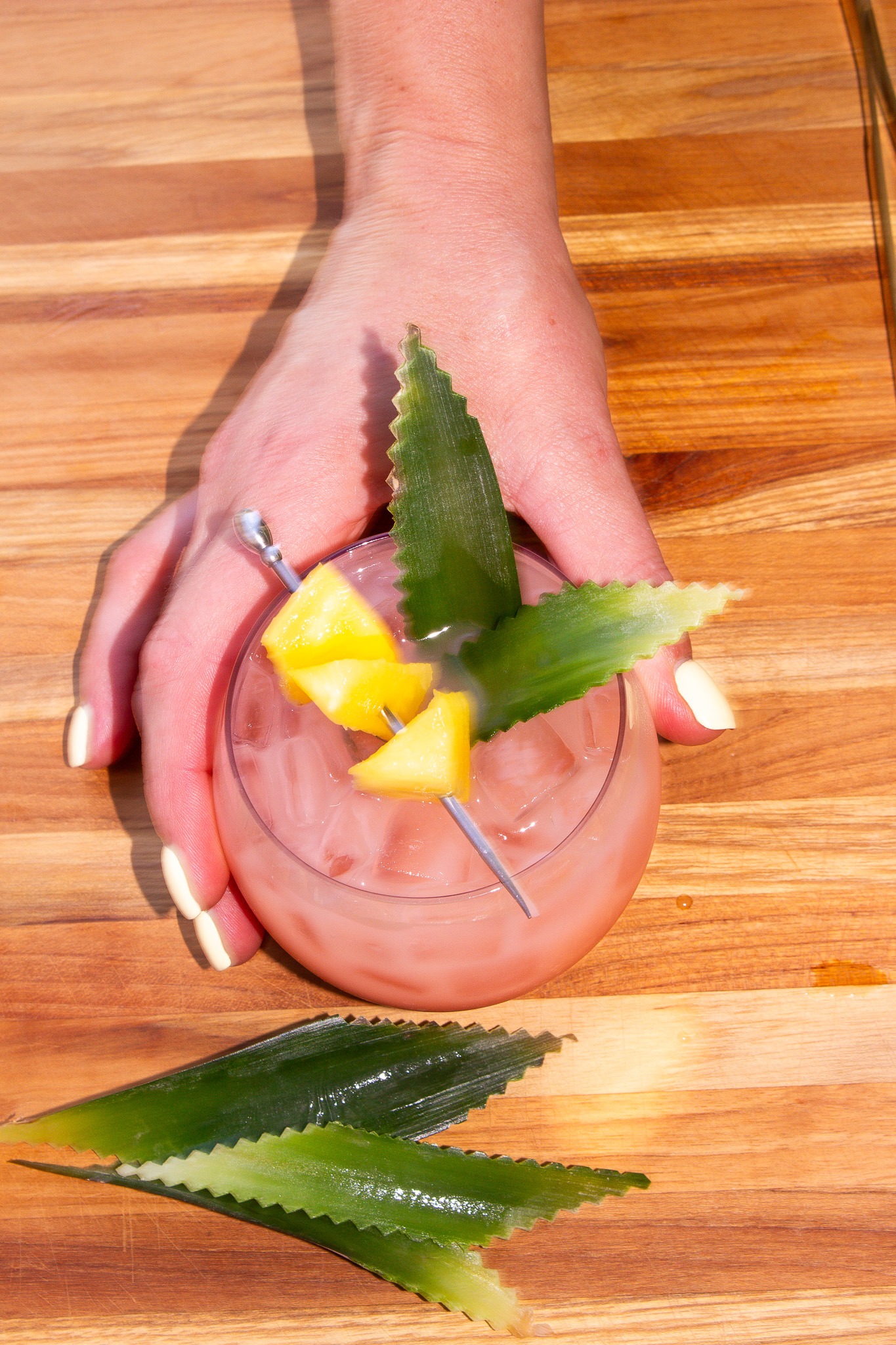 A hand finishing a pink House Pour cocktail with pineapple garnish