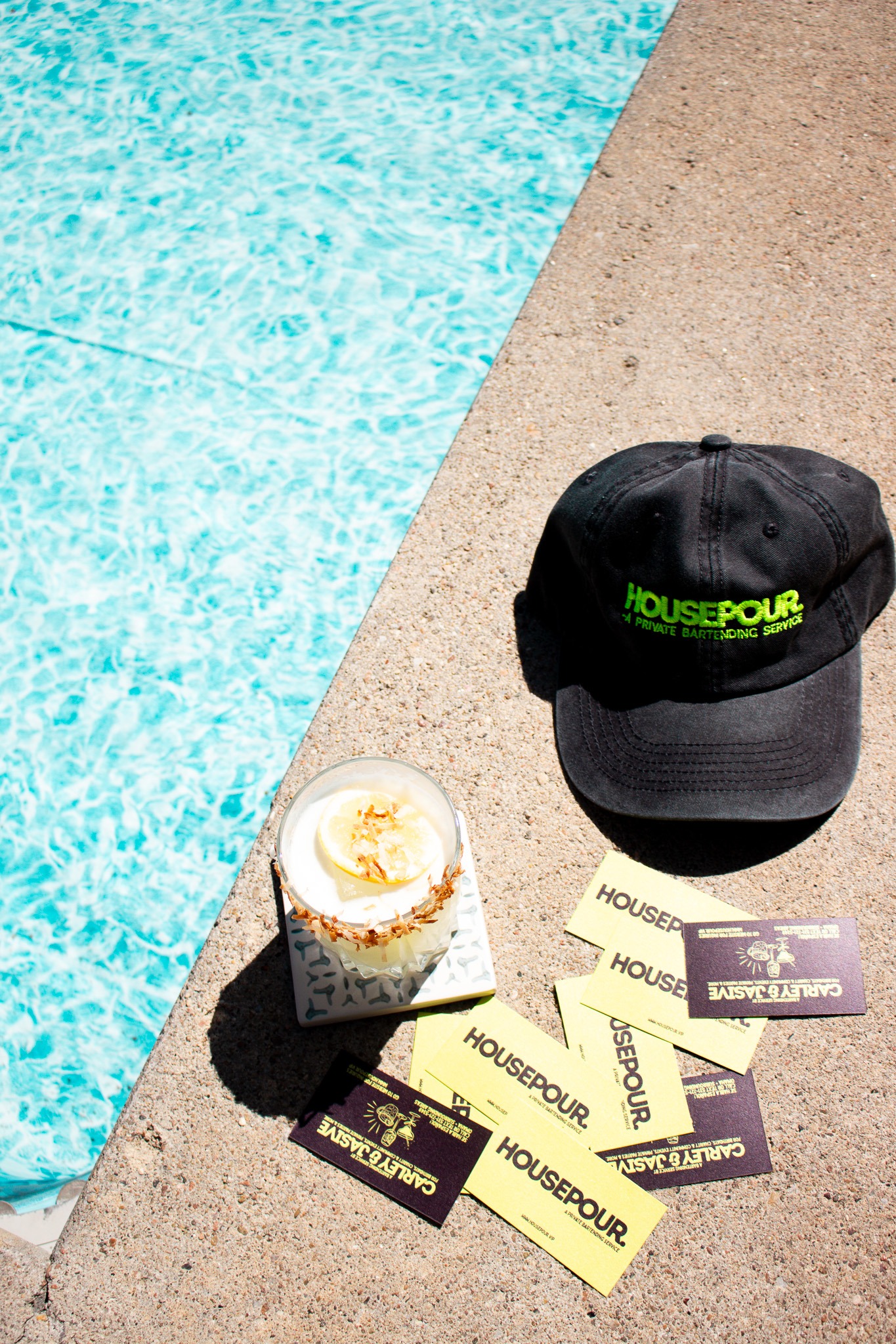 House Pour cocktail, hat and cards by a swimming pool